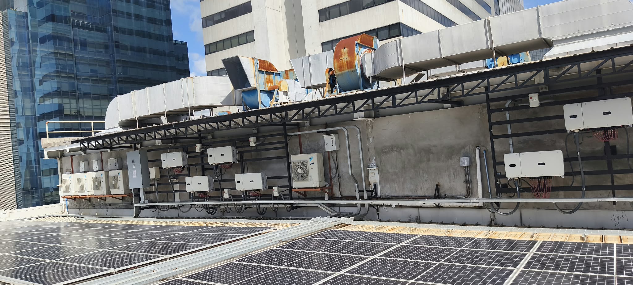Wide rooftop view showing solar panels and inverter equipment along a building.