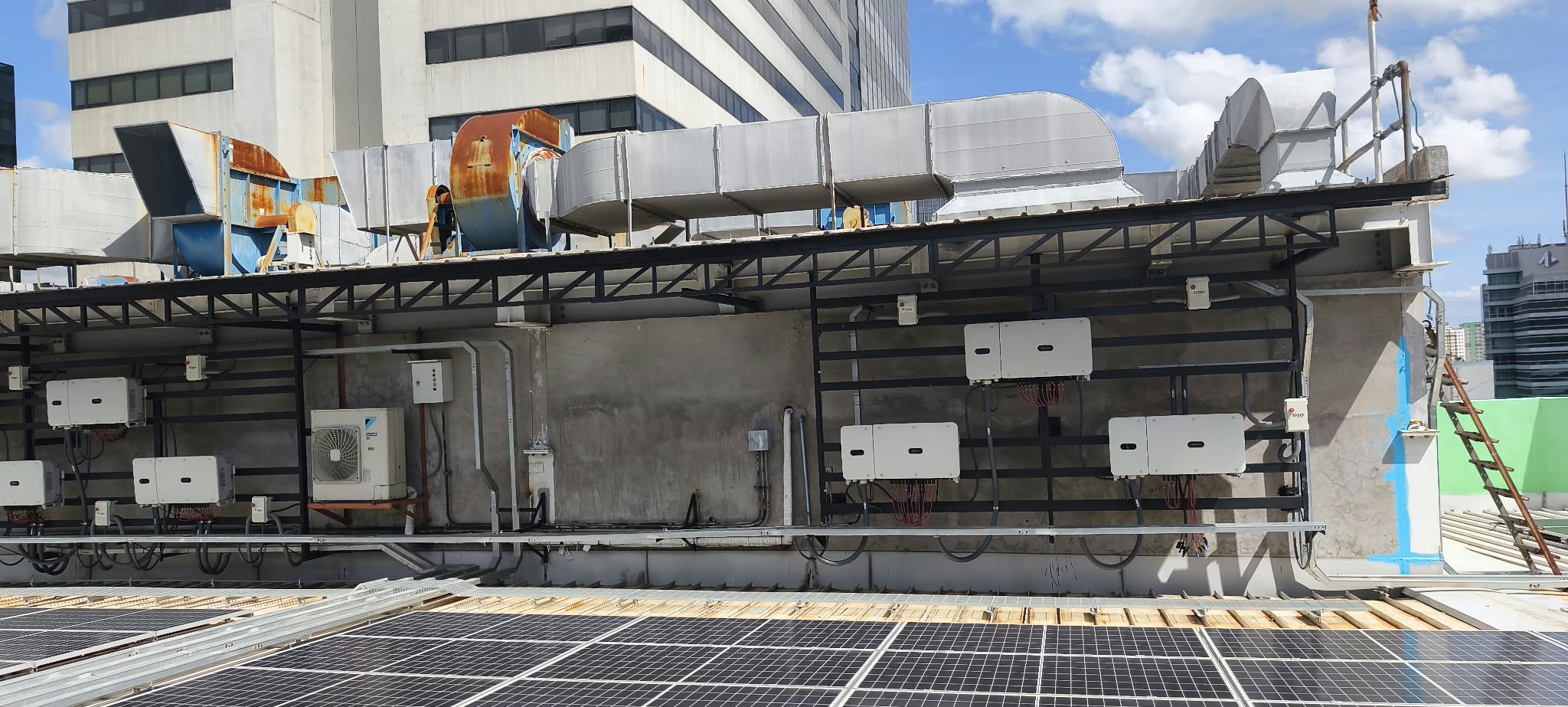 Commercial rooftop solar panels and multiple inverters under a canopy.