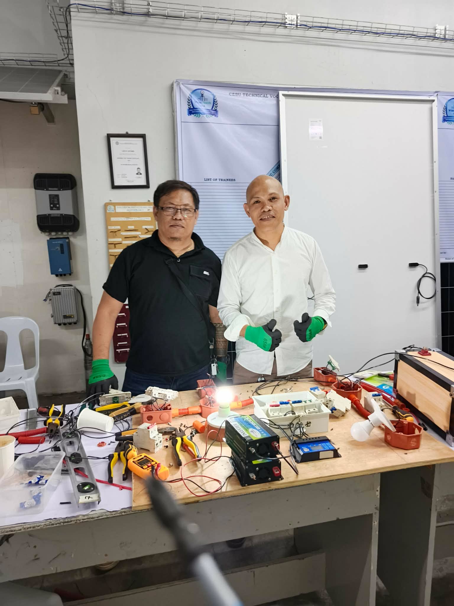 Two people reviewing electrical equipment around a workbench.