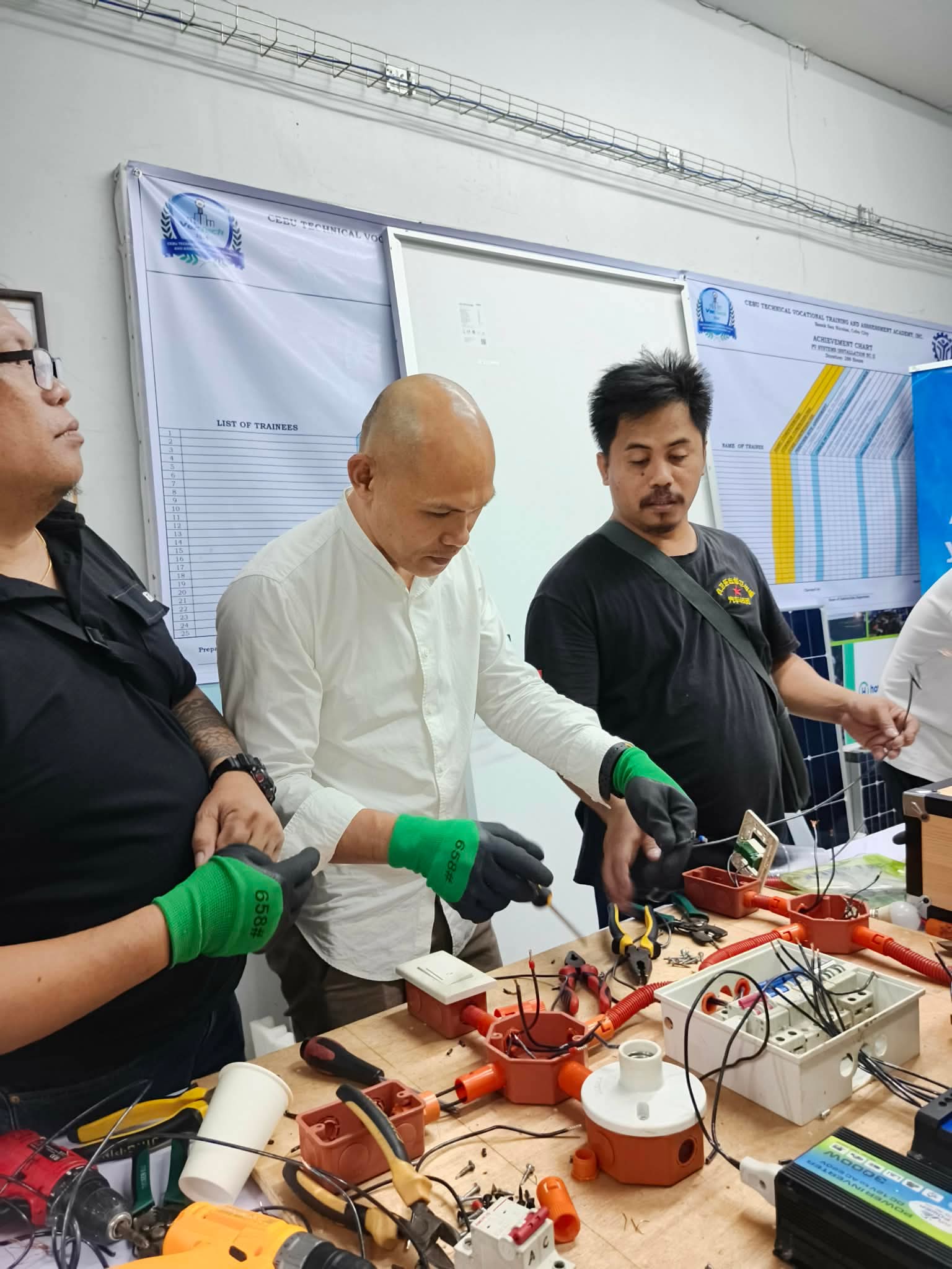 Trainees practicing wire connections with tools and safety gloves