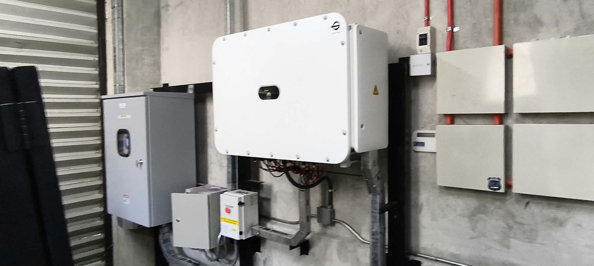 Wall-mounted hybrid inverter and electrical equipment beside solar panels.